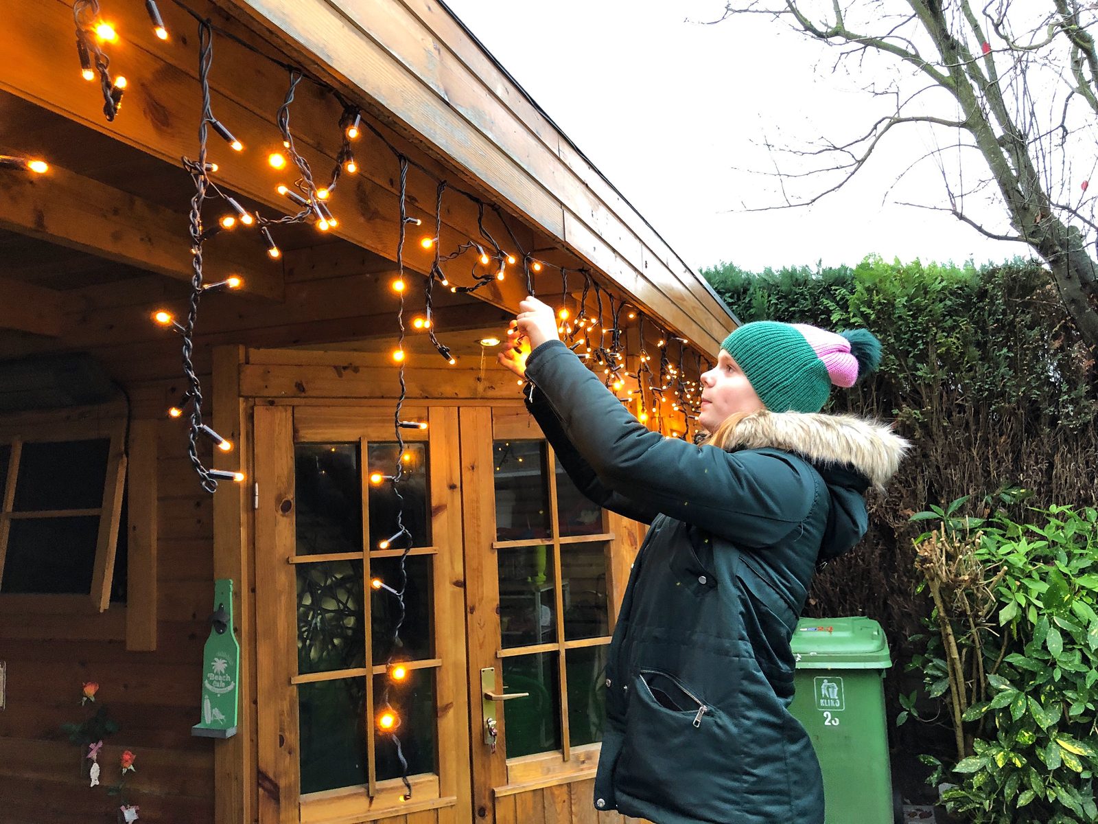 Installer clipping warm white holiday lights above a lit Napa entryway