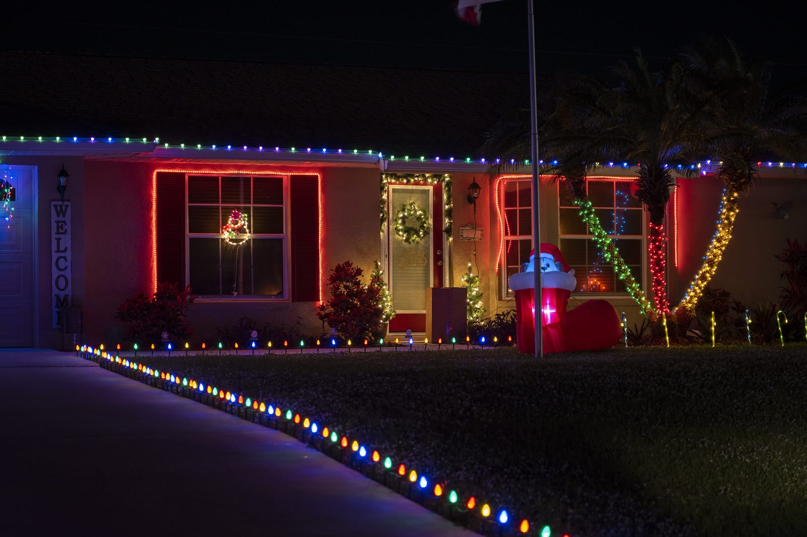 Front yard Christmas light display with wrapped trees and walkway lighting