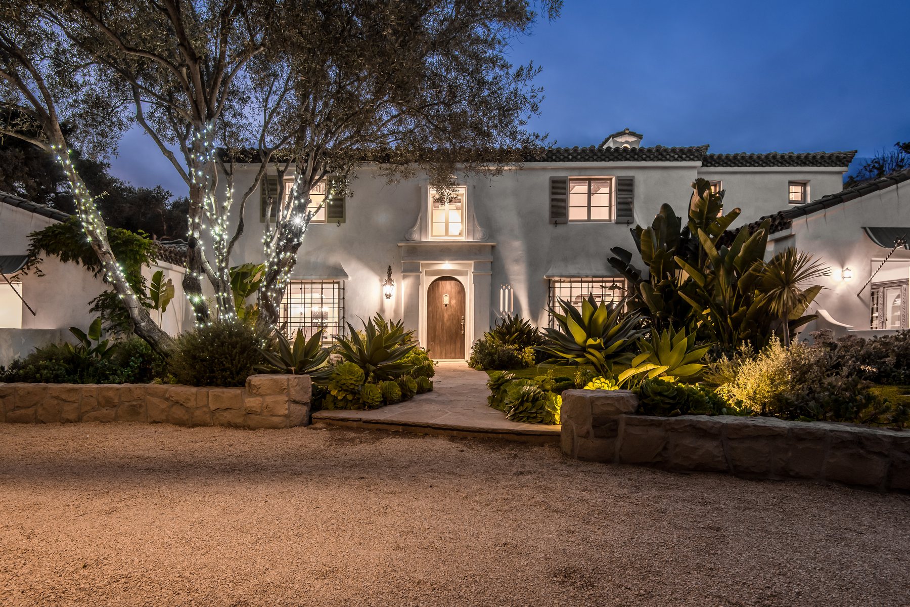 Stucco estate at twilight with wrapped trees and warm lighting
